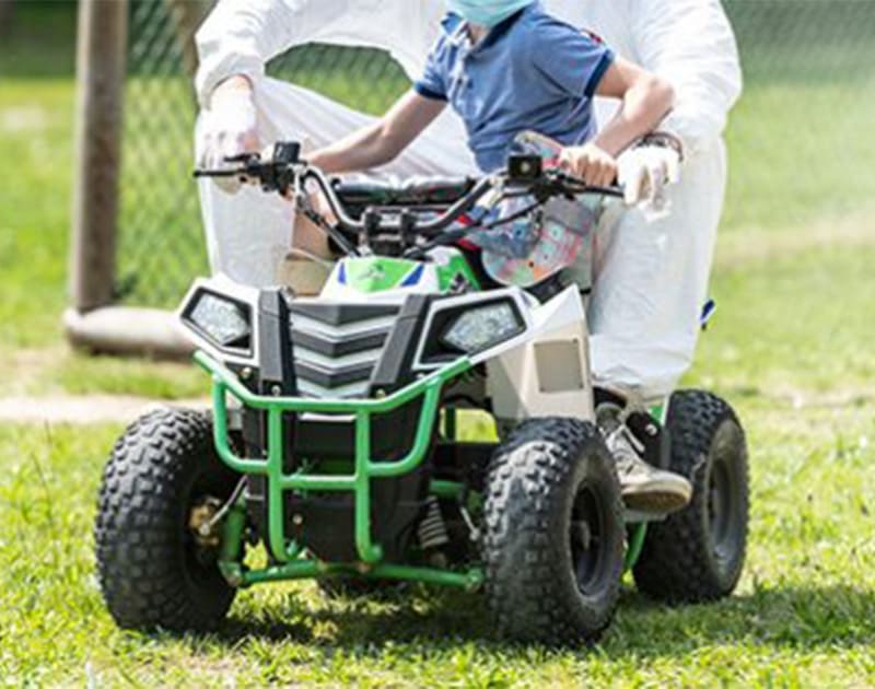 A kid learning how to drive a small ATV with a parent