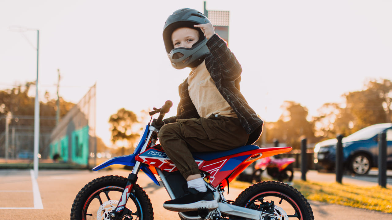 A kid riding on a mini dirt bike with protective helmet
