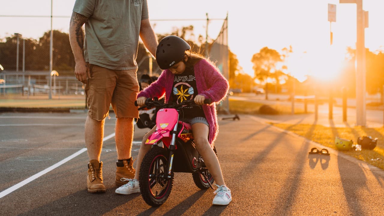An adult teaching a kid dirt bike rider to ride